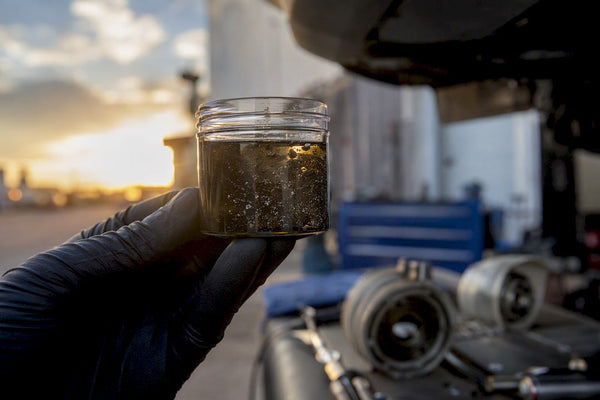 Hand holding container of Haldex fluid with metal flakes